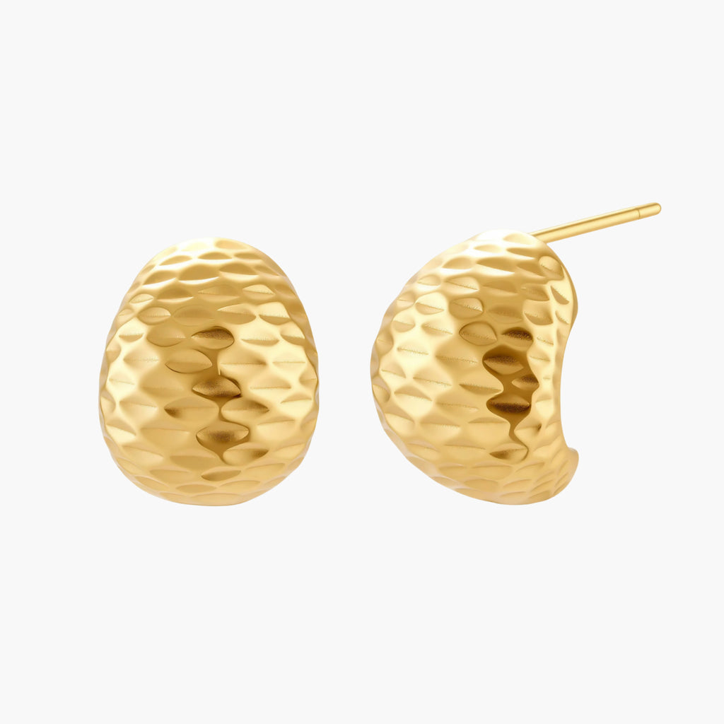 Pair of textured gold-plated sterling silver huggie earrings with dimpled surface finish on cream background.