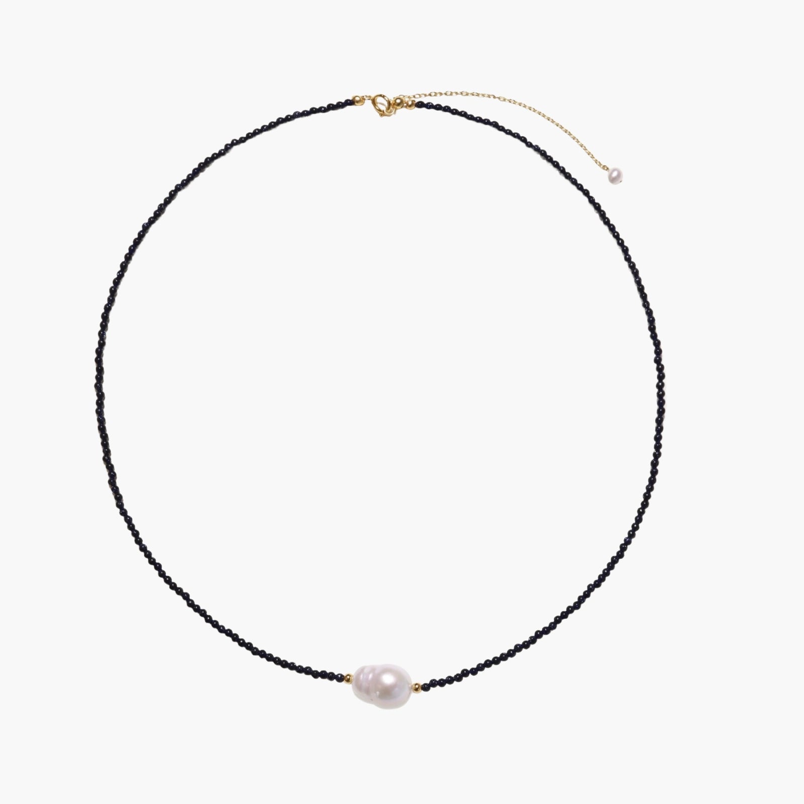 Delicate necklace with black blue sandstone beads and baroque pearl center on white background with gold accents.