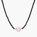 Beaded black agate necklace with iridescent baroque freshwater pearl centerpiece on cream background.