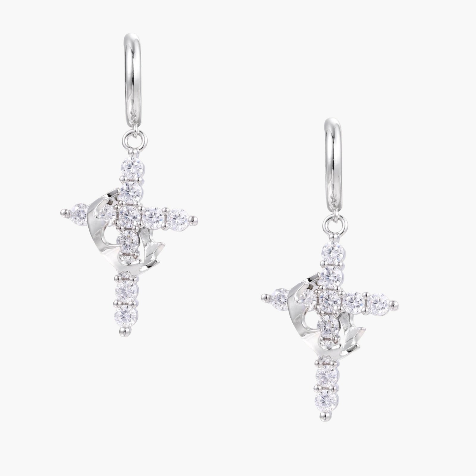 White gold-plated hoop earrings with sparkling zirconia cross charms dangling against cream background