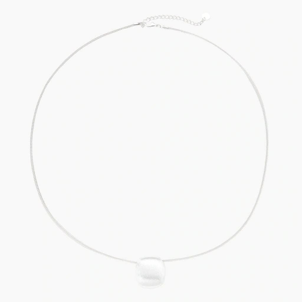 Minimalist brushed sterling silver dome pendant on delicate chain against cream background, showing matte textured finish