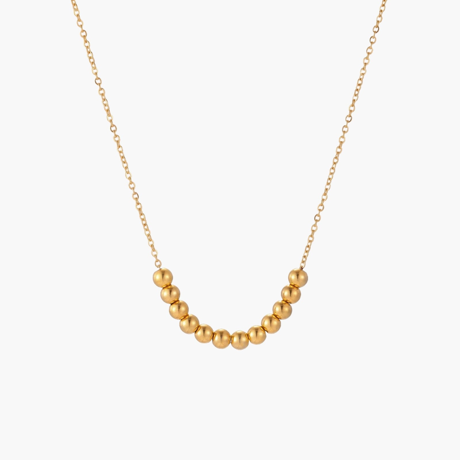 Delicate gold-plated necklace with graduated spherical beads forming gentle smile curve on beige background
