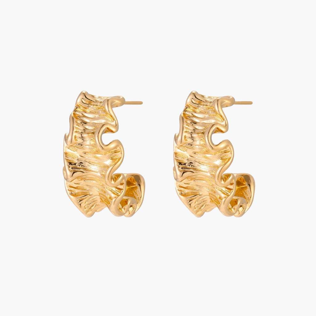 Pair of gold huggie hoops with sculpted wave texture and dimensional ripples on neutral background.