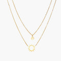 Gold layered necklace set with sunburst and smiley face pendants on delicate chains against white background.
