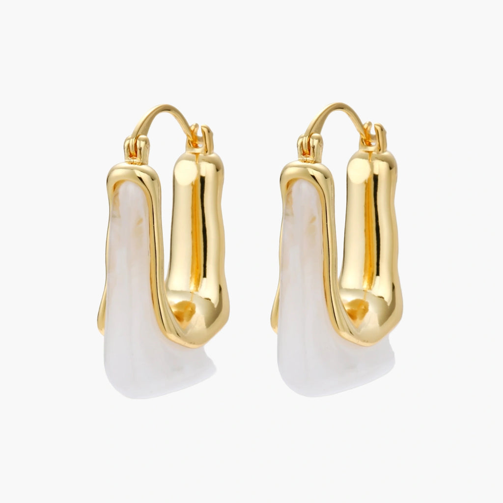 Sculptural gold-plated hoop earrings with flowing curved design and lever-back closure on cream background.
